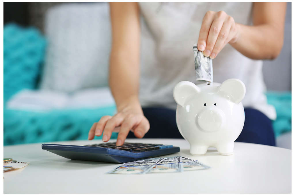 Female hand putting money into piggy bank and counting on calculator