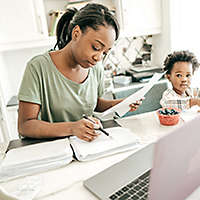 Mother doing paperwork; child in a highchair in the kitchen