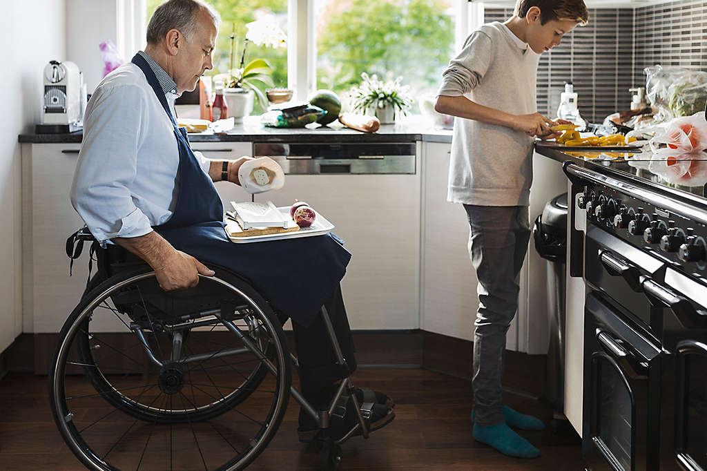 An older man in a wheelchair and a young boy preparing food in a kitchen.
