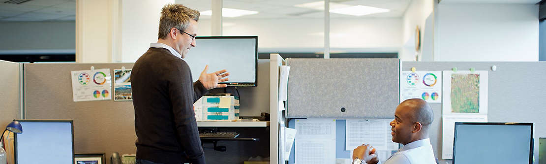 Two men talking at their cubicles at work.