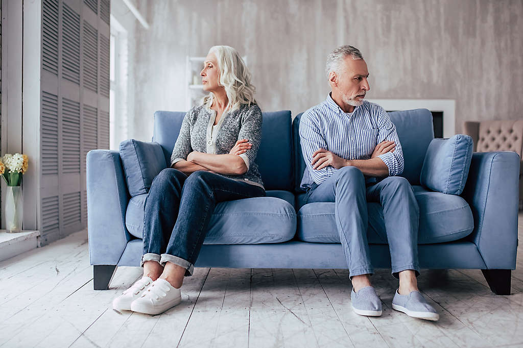 Upset senior couple sitting on sofa together and looking to opposite sides with arms crossed