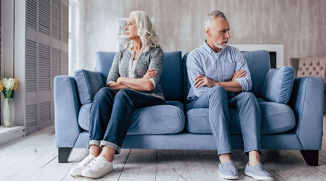 Upset senior couple sitting on sofa together and looking to opposite sides with arms crossed