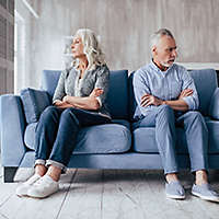 Upset senior couple sitting on sofa together and looking to opposite sides with arms crossed