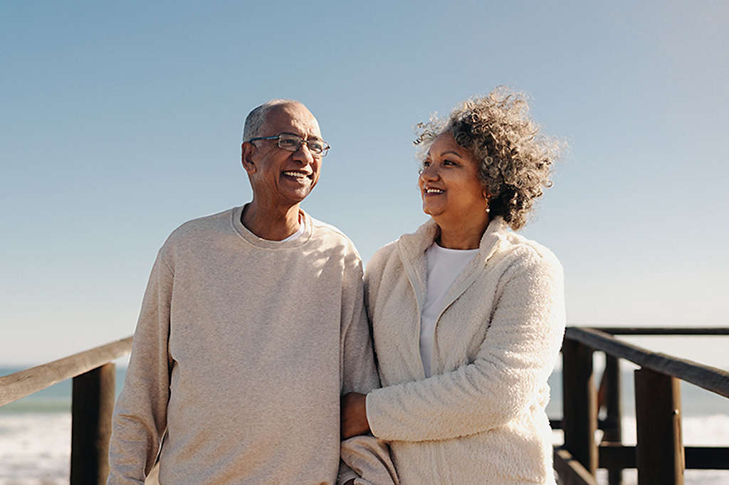 Mature couple smiling happily while taking a walk along a wooden foot bridge at the beach