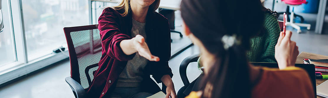 A woman in an office sitting down having a conversation with another woman.