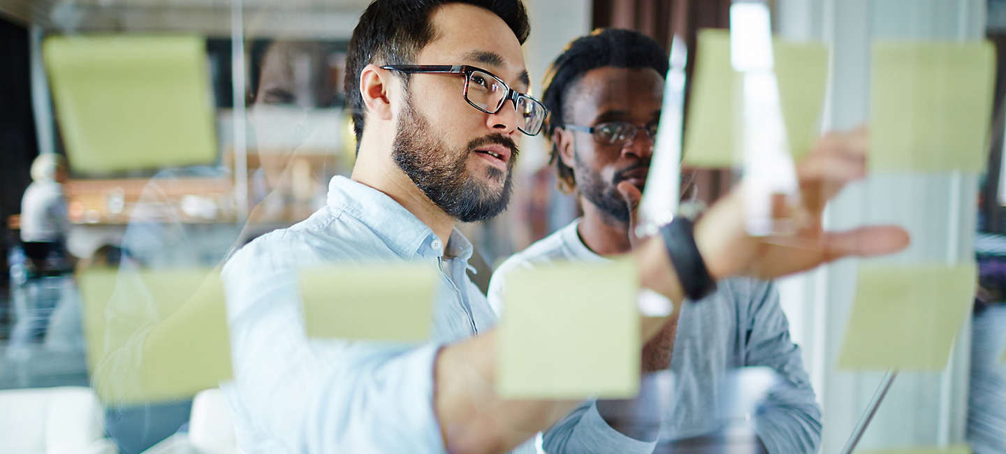 Two employees looking at sticky notes on whiteboard