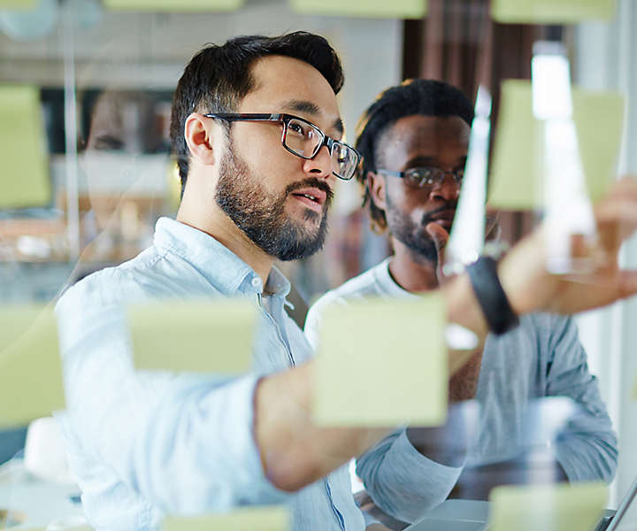 Two employees looking at sticky notes on whiteboard