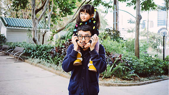 A father holding his young daughter on his shoulders