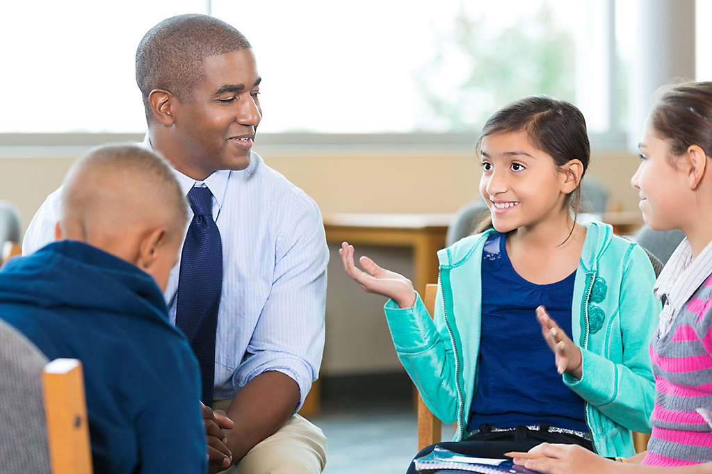 A teacher listening to a group of young students. 