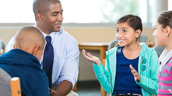 A teacher listening to a group of young students.