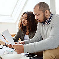 Two people sitting on a couch reviewing paperwork.