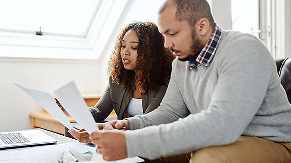 Young couple sitting on a couch reviewing paperwork.