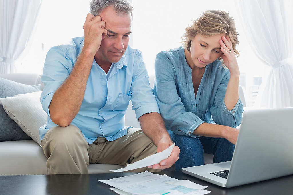 Worried couple paying their bills online with laptop at home in the living room