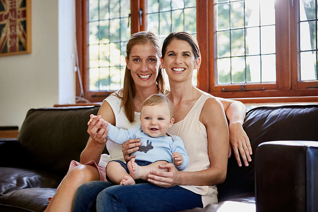 Happy couple with baby boy sitting on sofa at home