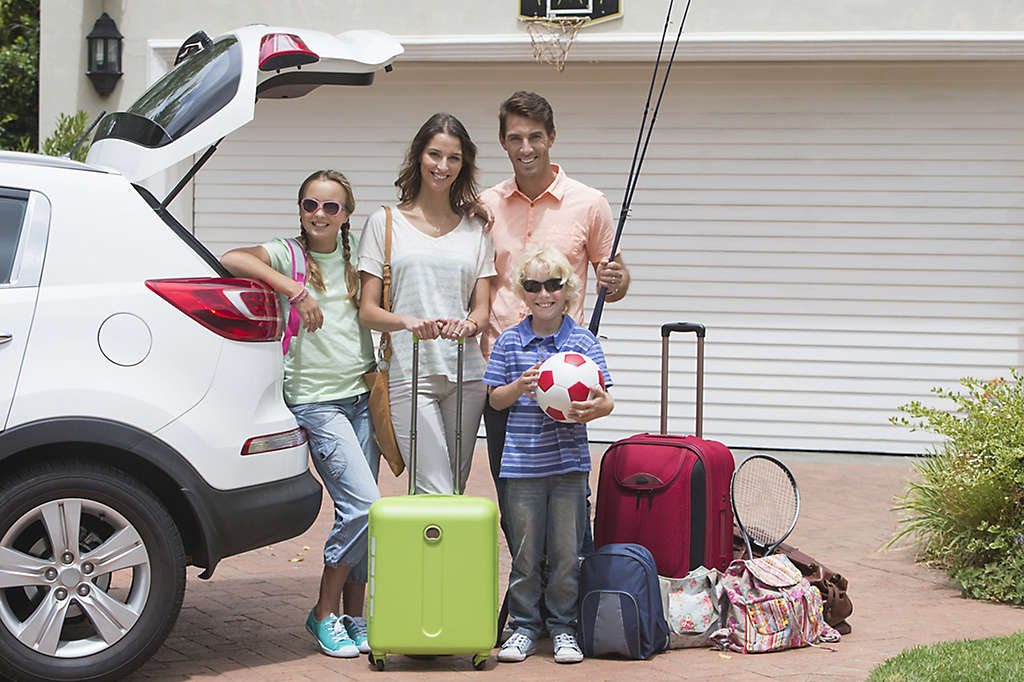 Parents with two children smiling packing car in sunny driveway