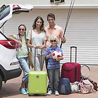 Parents with two children smiling packing car in sunny driveway