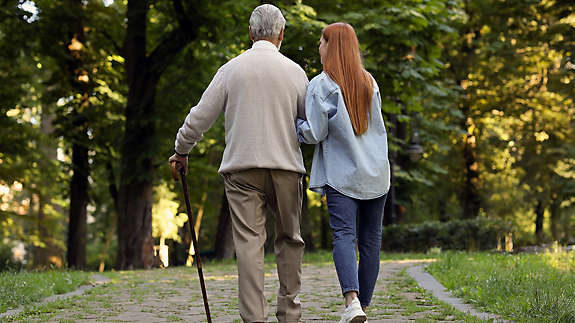 A woman helping an eldery man walk.