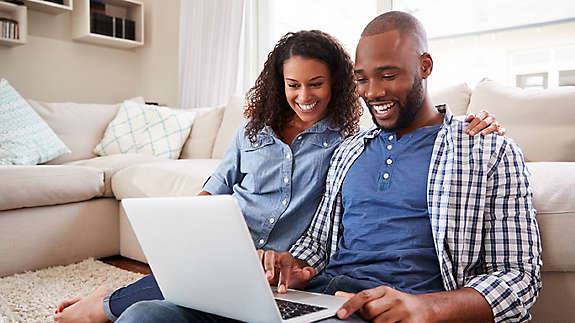 Young couple using laptop sitting on the floor at home