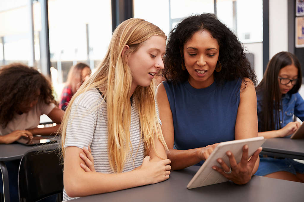 mentor helps teenage schoolgirl with tablet computer