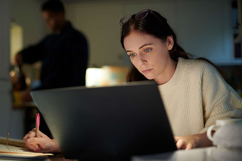 Woman working late on laptop and taking notes