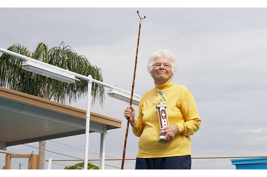 Older woman outside holding shuffleboard stick and trophy.