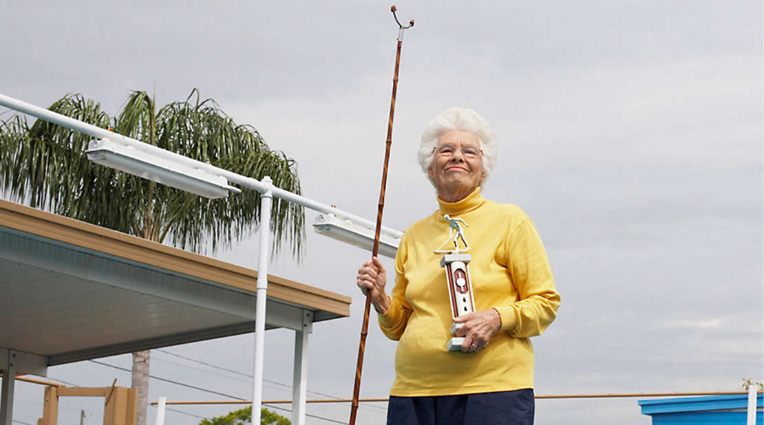Older women outside holding shuffle board stick and trophy