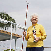 Older woman outside holding shuffleboard stick and trophy.