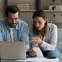 Serious millennial spouses engaged in housekeeping manage family finances discuss budget. Concentrated young couple husband wife sit on sofa at home office talk study receipts calculate loan payments