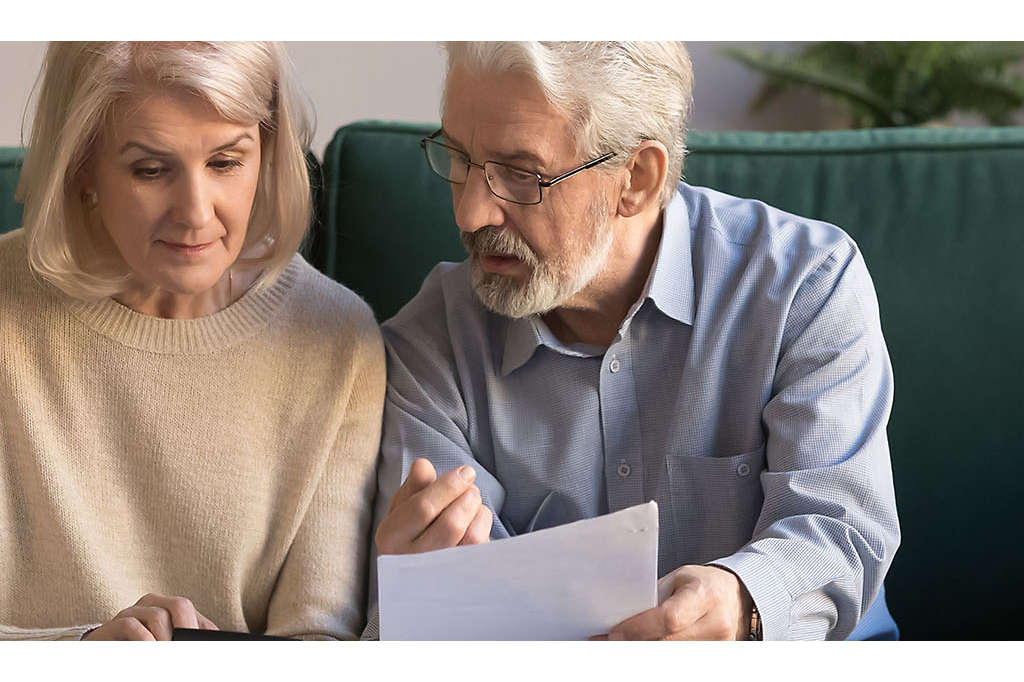 A mature couple siting on the couch looking a paperwork.