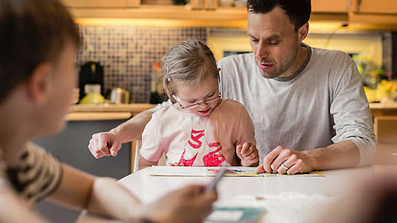 Father teaching daughter with son in foreground at home