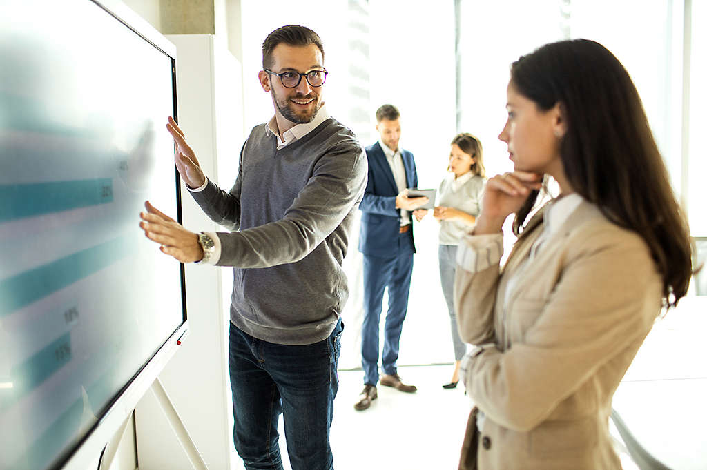 2 employers gathered around a large screen analyzing data