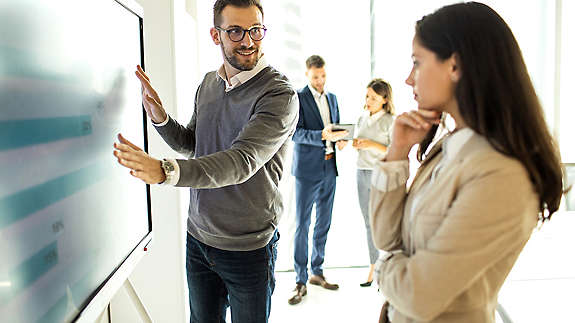 2 employers gathered around a large screen analyzing data