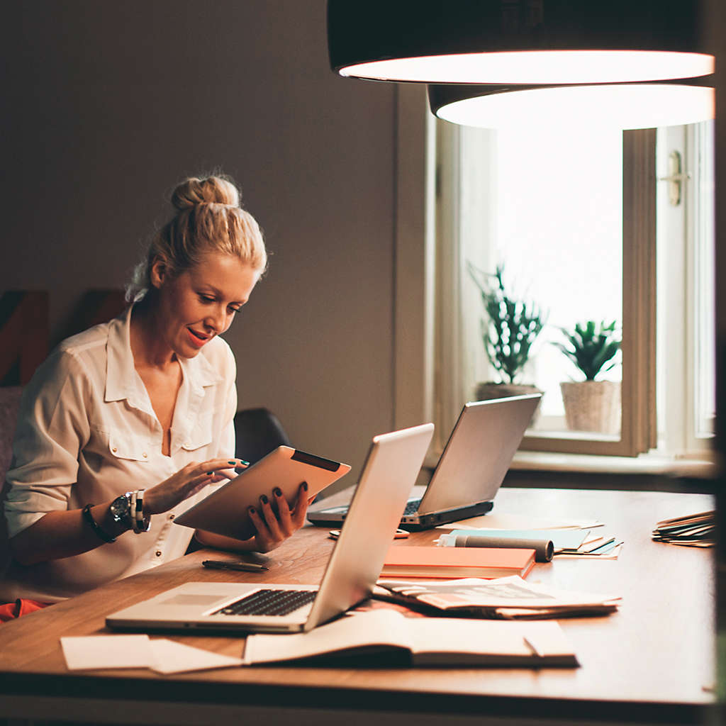 A woman sitting at her desk looking at something on her tablet.