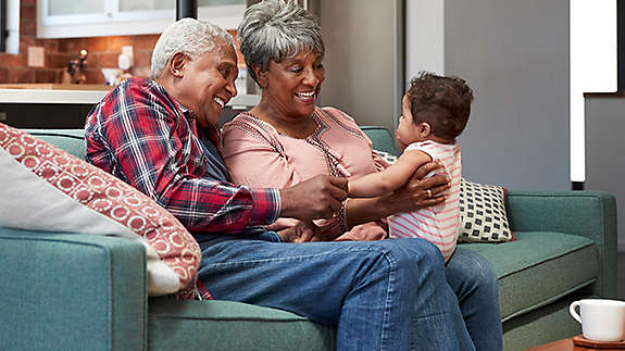 Two older adults playing with a toddler on a sofa