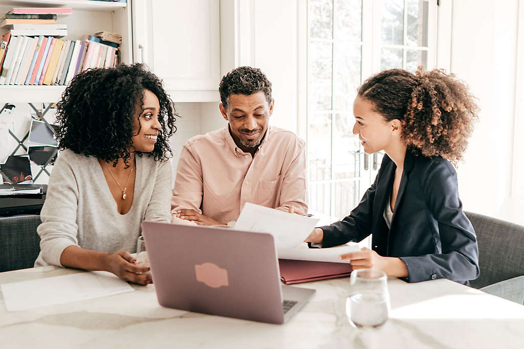 A couple sitting at a table looking at paperwork and talking to an agent.