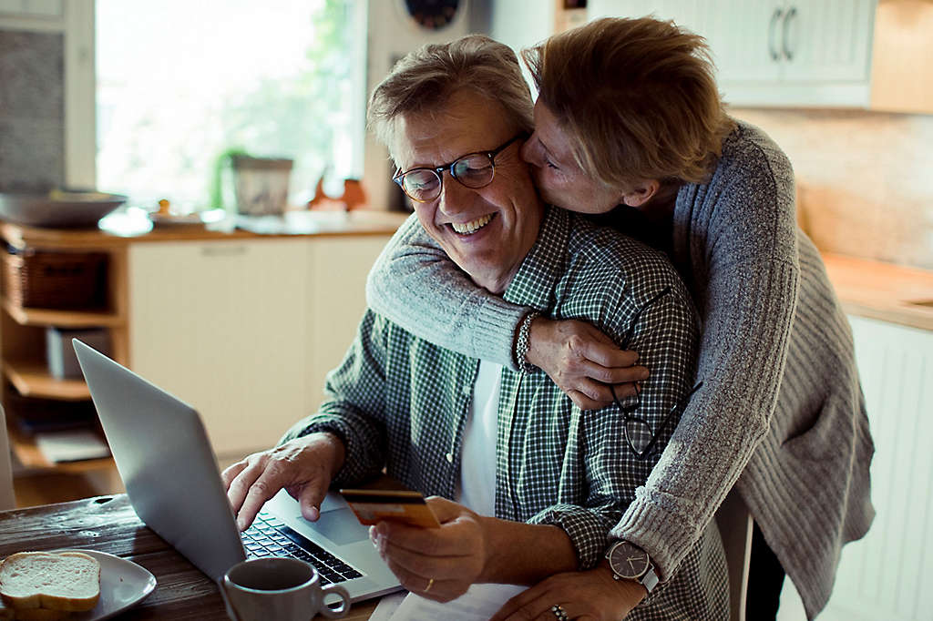 A mature couple kissing while the husband is using his computer.