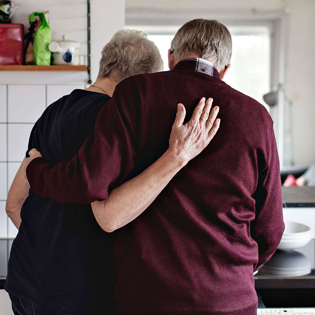An elderly couple hugging in the home.