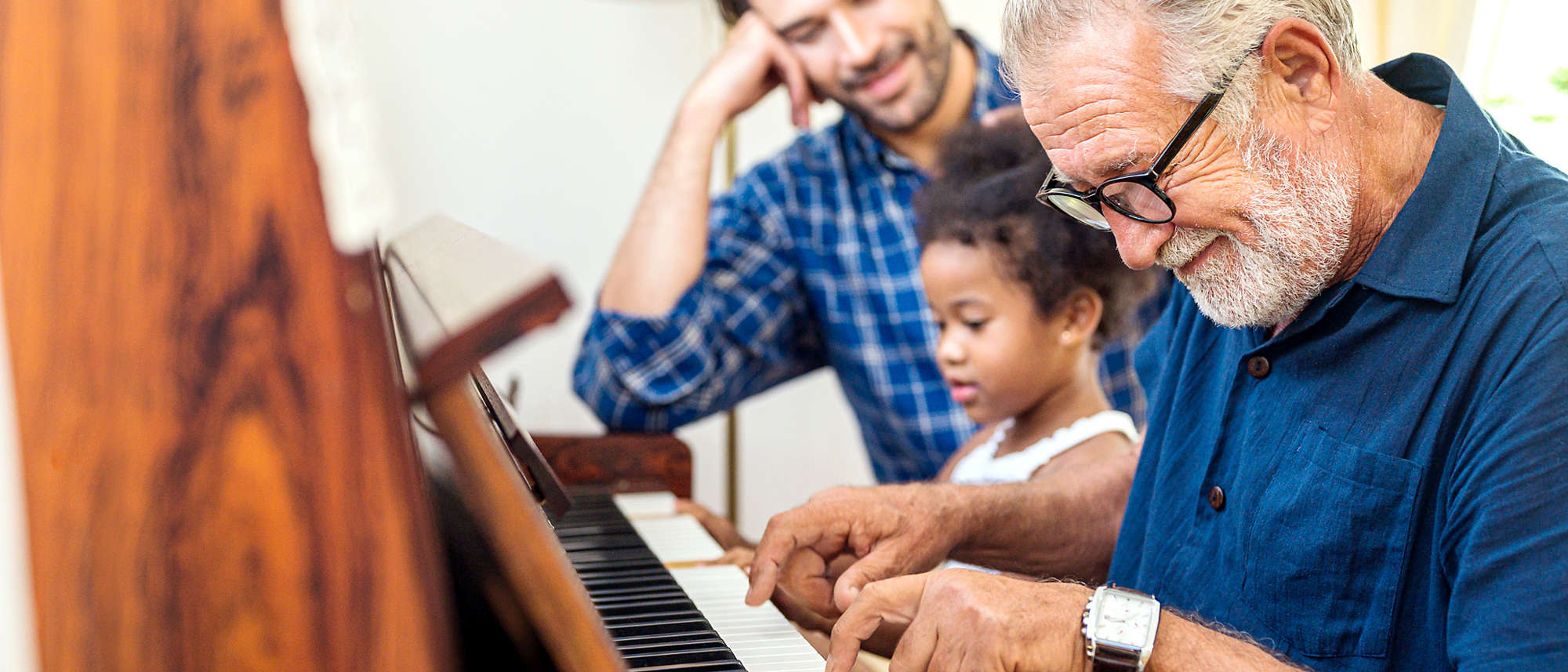 Grandfather playing piano with his granddaughter and son in living room