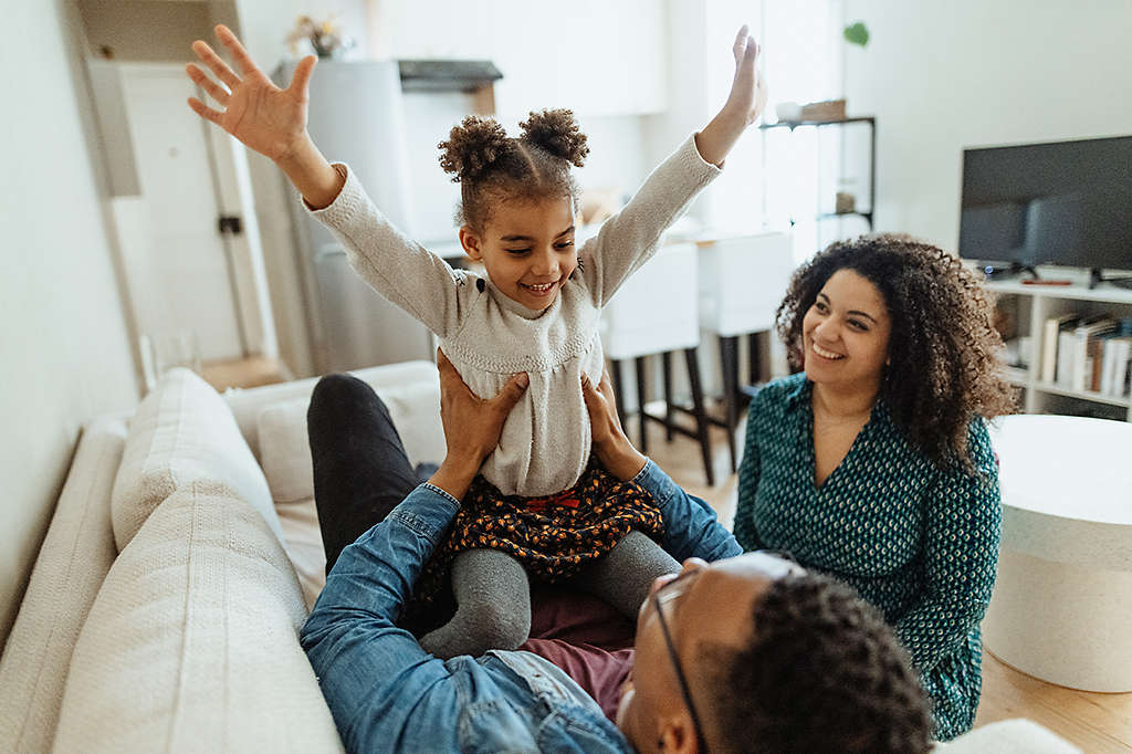 happy mother and father enjoying time at home playing on the couch with daughter