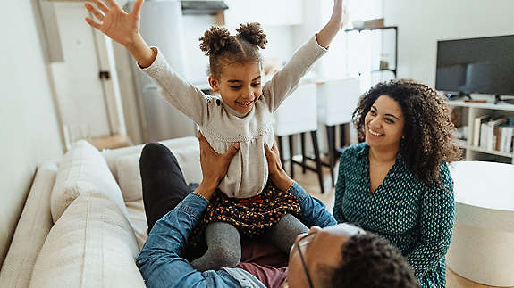happy mother and father enjoying time at home playing on the couch with daughter