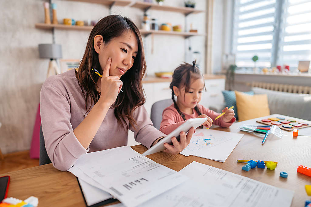 mother checking her finances on tablet while her daughter is playing next to her