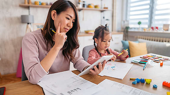 mother checking her finances on tablet while her daughter is playing next to her