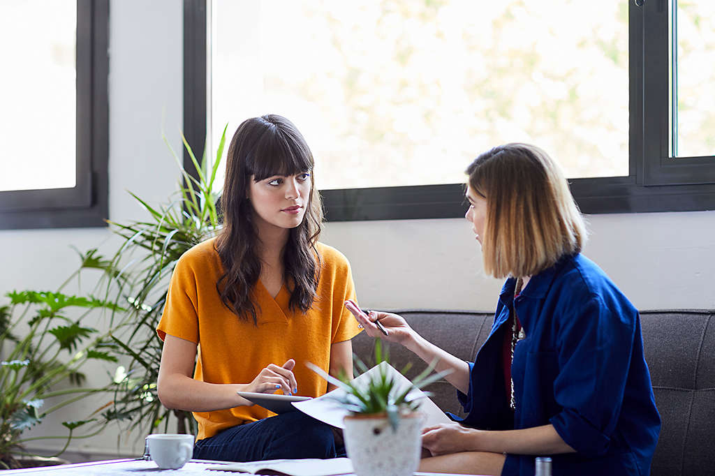 two female coworkers in a discussion while sitting on a couch