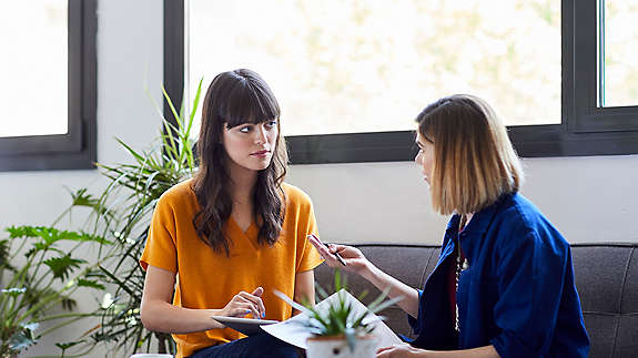 two female coworkers in a discussion while sitting on a couch