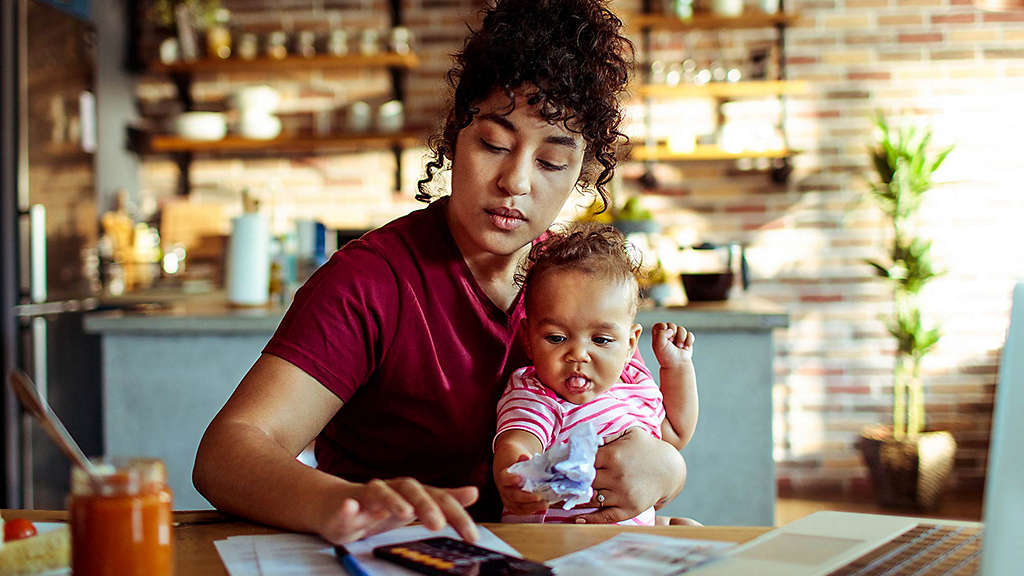 Woman sitting at desk holding baby while tapping on phone.