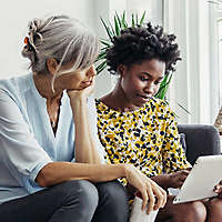 Two women sitting on couch looking at tablet together.