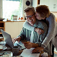 Man working on computer while wife gives him a kiss on the cheek.