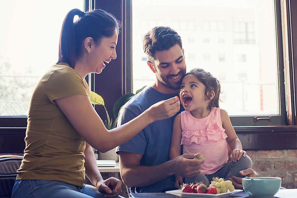 Young parents feeding daughter vegetables.