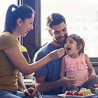 Young parents feeding daughter vegetables.