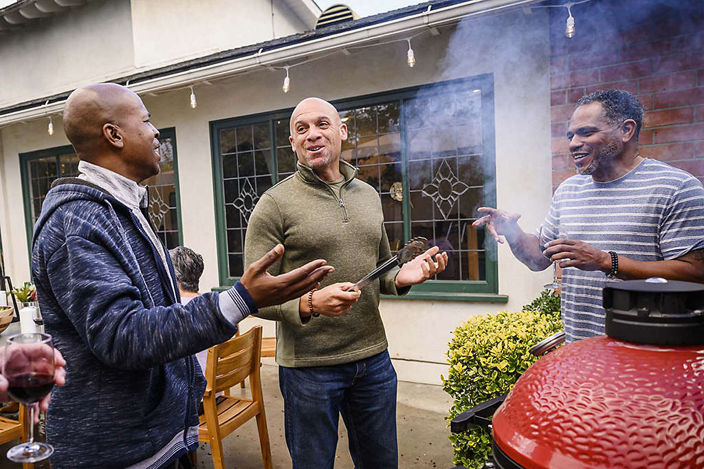 Three men talking while grilling at a barbecue.